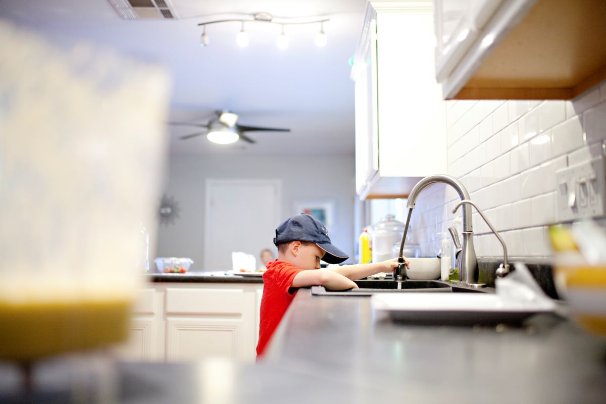 A boy is rinsing dishes with the sprayer on the kitchen faucet