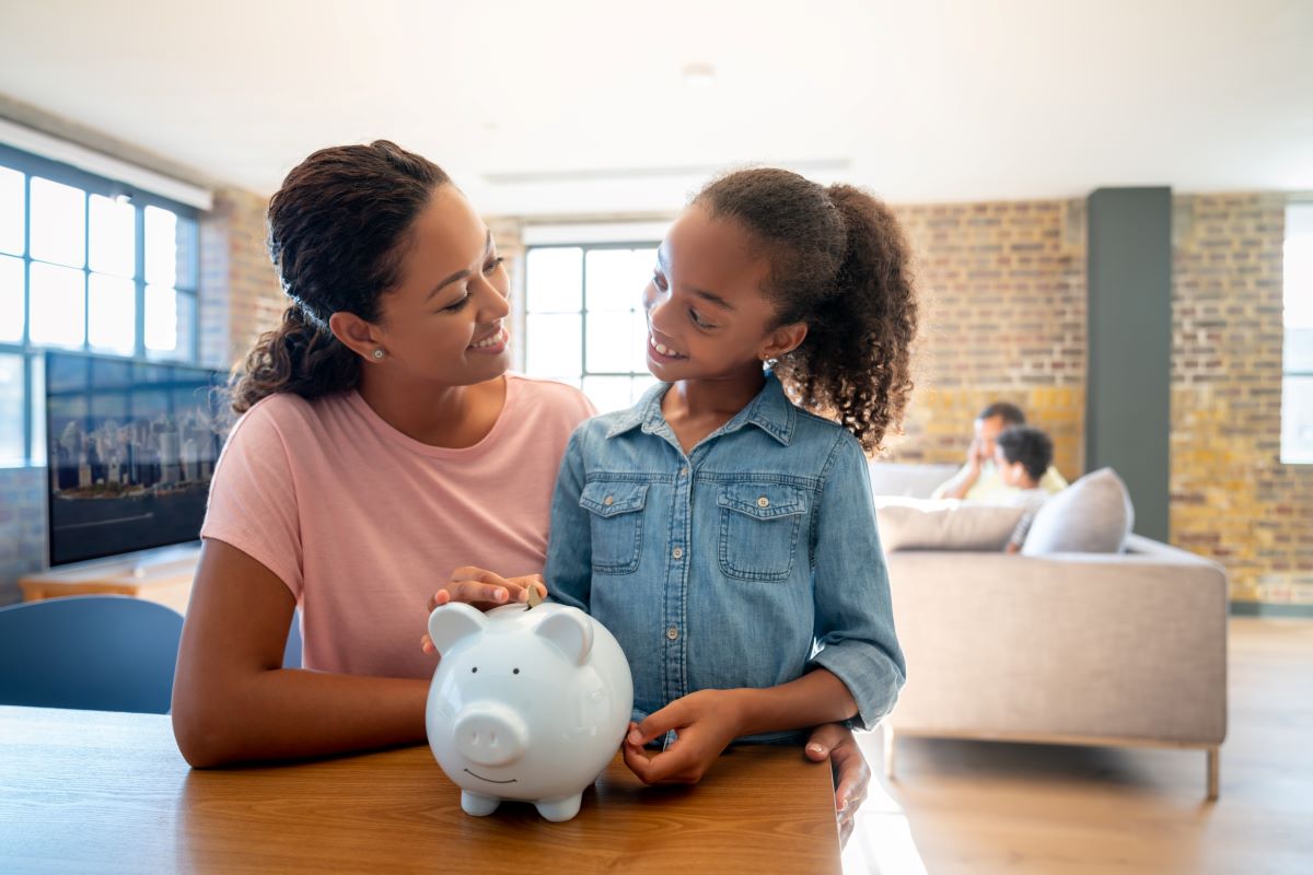 Daughter placing money in piggy bank as the mom watches