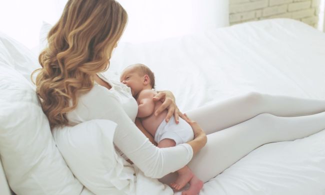 Mom breastfeeding newborn in bed.
