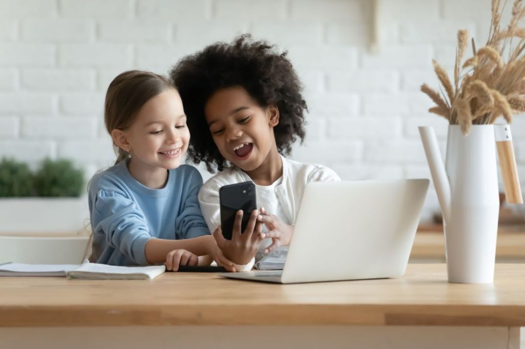 Two girls sharing a cellphone in front of a laptop