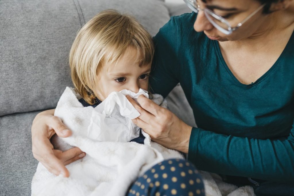Parent taking care of a sick child, helping them blow their nose.