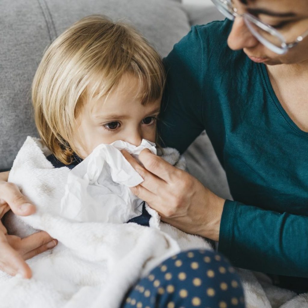 Parent taking care of a sick child, helping them blow their nose.