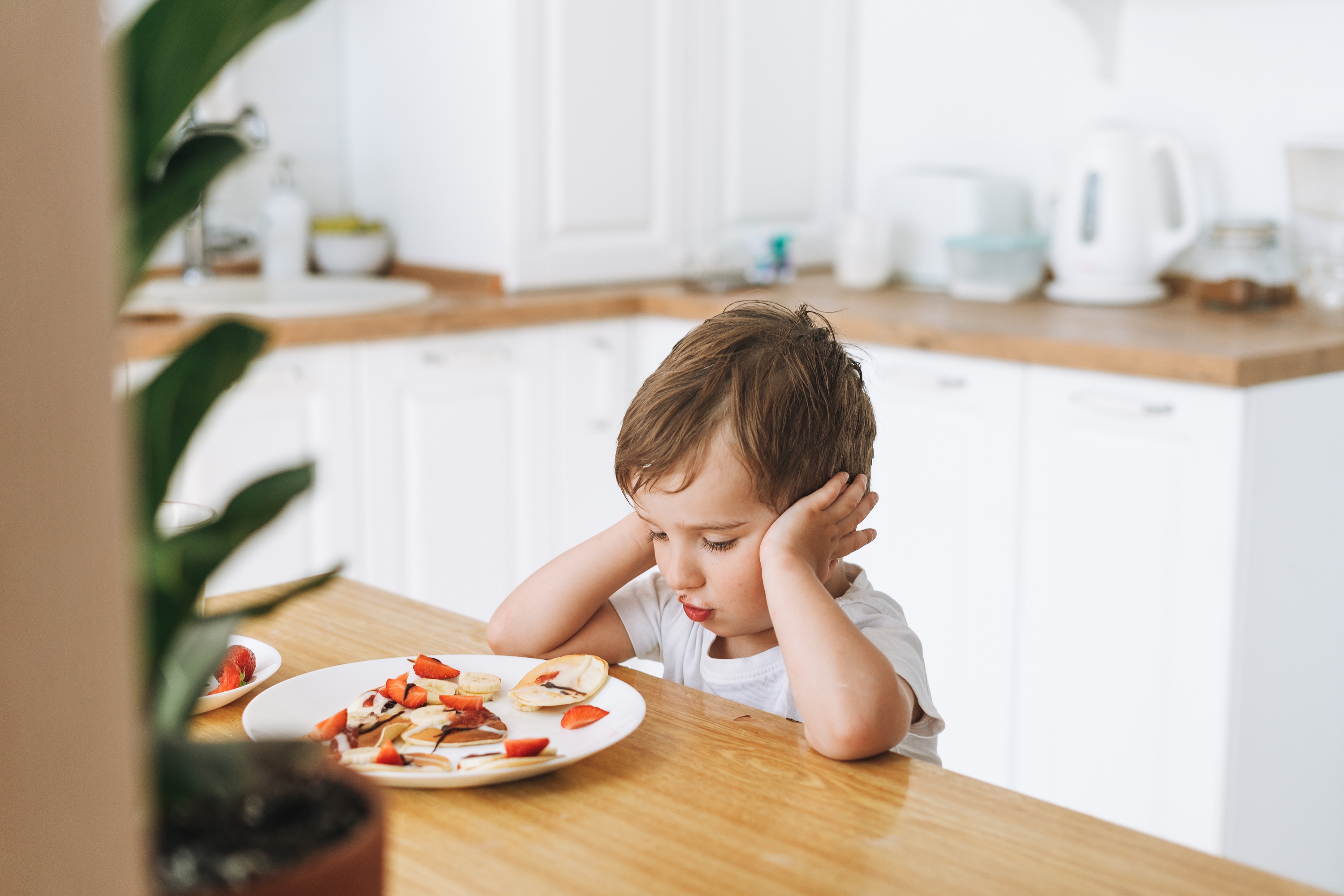 A toddler sitting down with a plate of food.