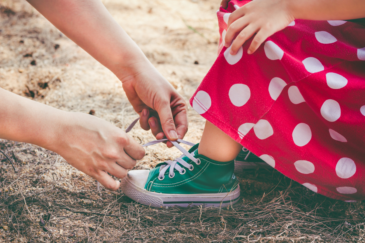 A parent teaching a toddler girls how to tie her sneaker