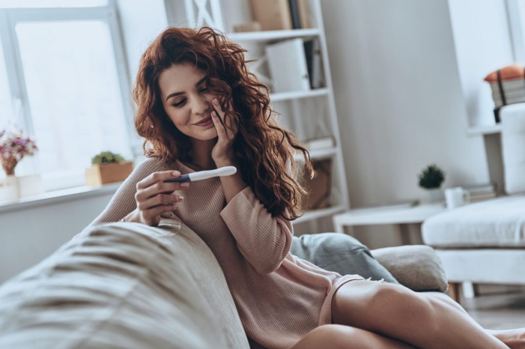 Woman sitting on couch and looking at a pregnancy test