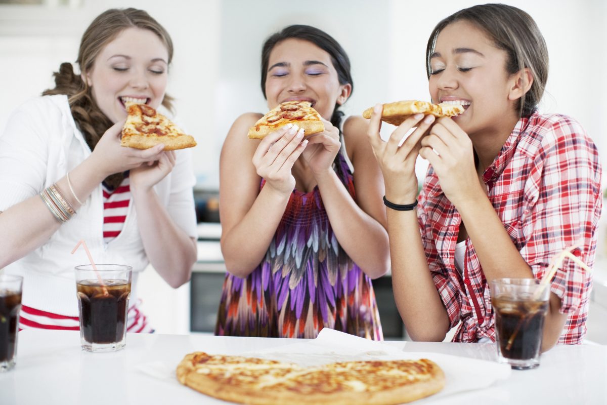 Teenage girls eating pizza happily together.