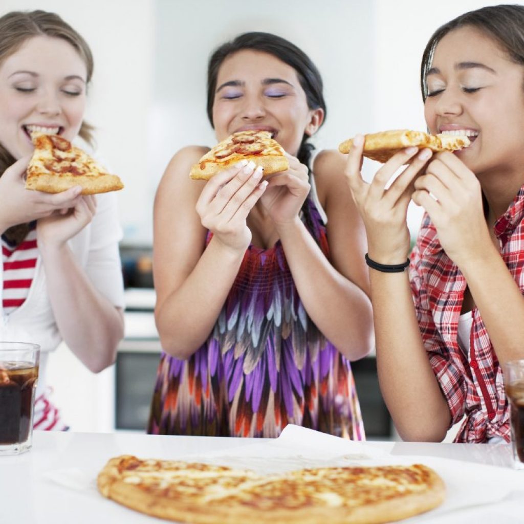 Teenage girls eating pizza happily together.