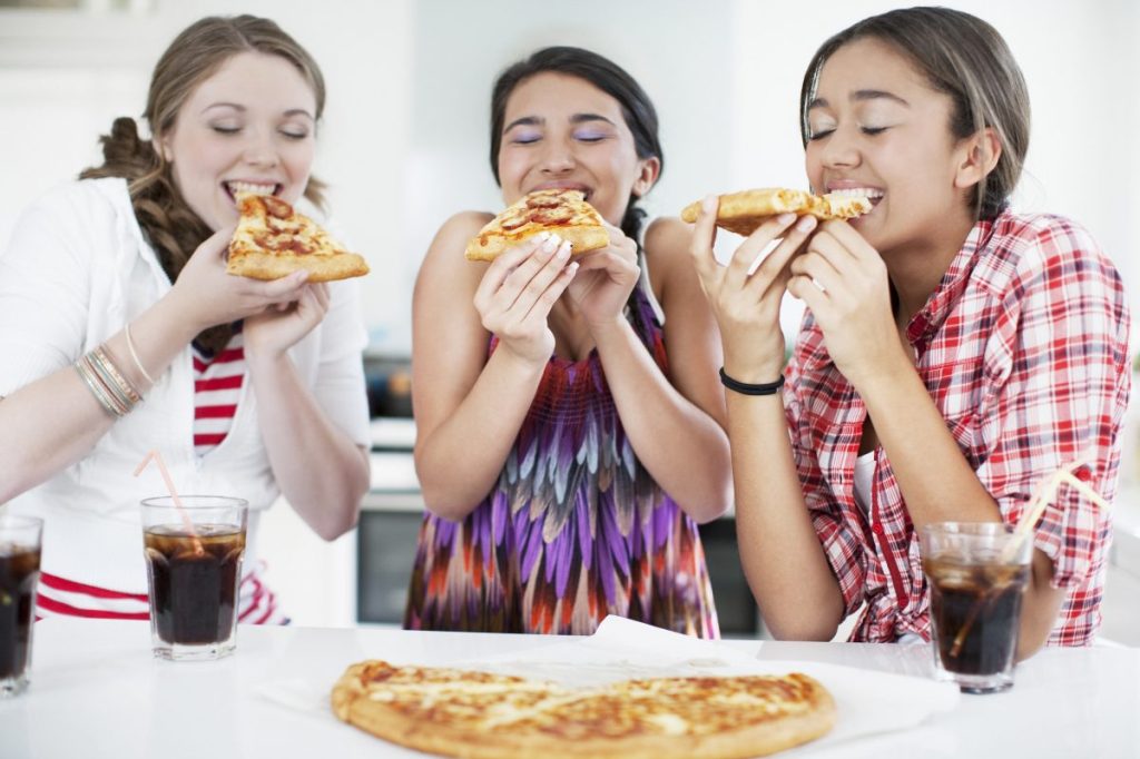 Teenage girls eating pizza happily together.