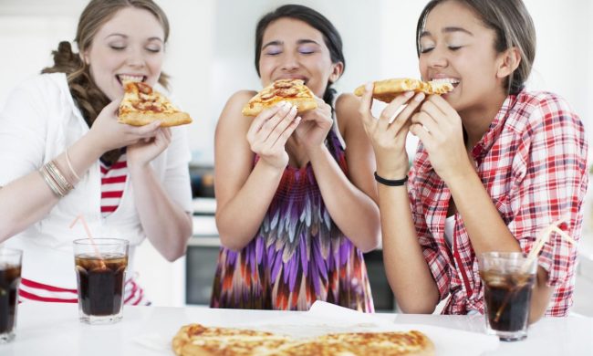 Teenage girls eating pizza happily together