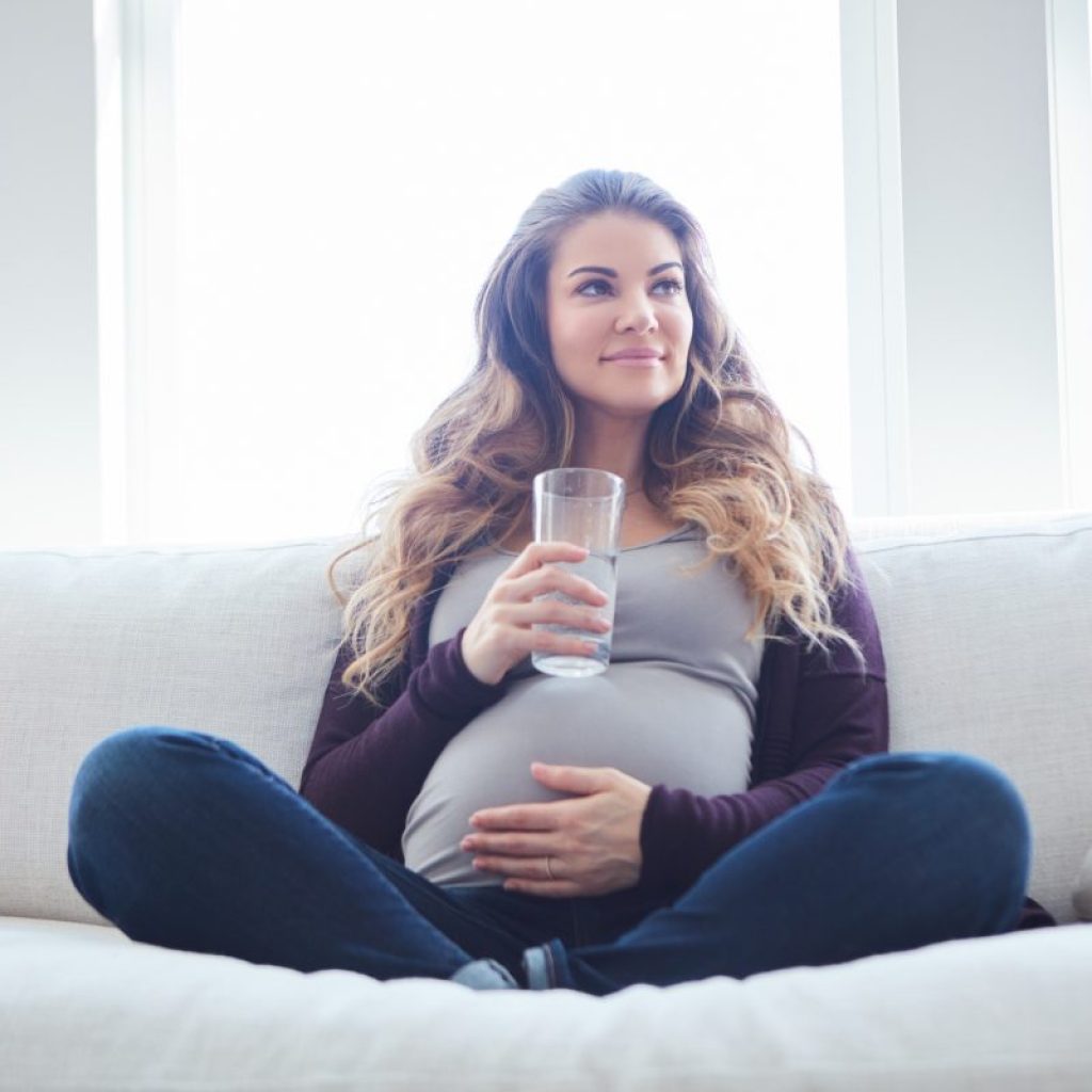 Pregnant woman drinking water while on the couch.