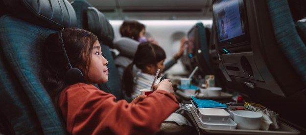 Little girl watching movie on the seat-back TV screen while enjoying her airline meal