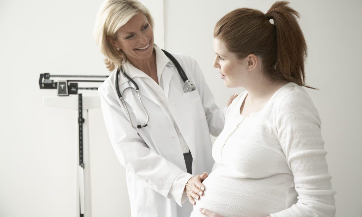 Female doctor touching pregnant woman's stomach, smiling.