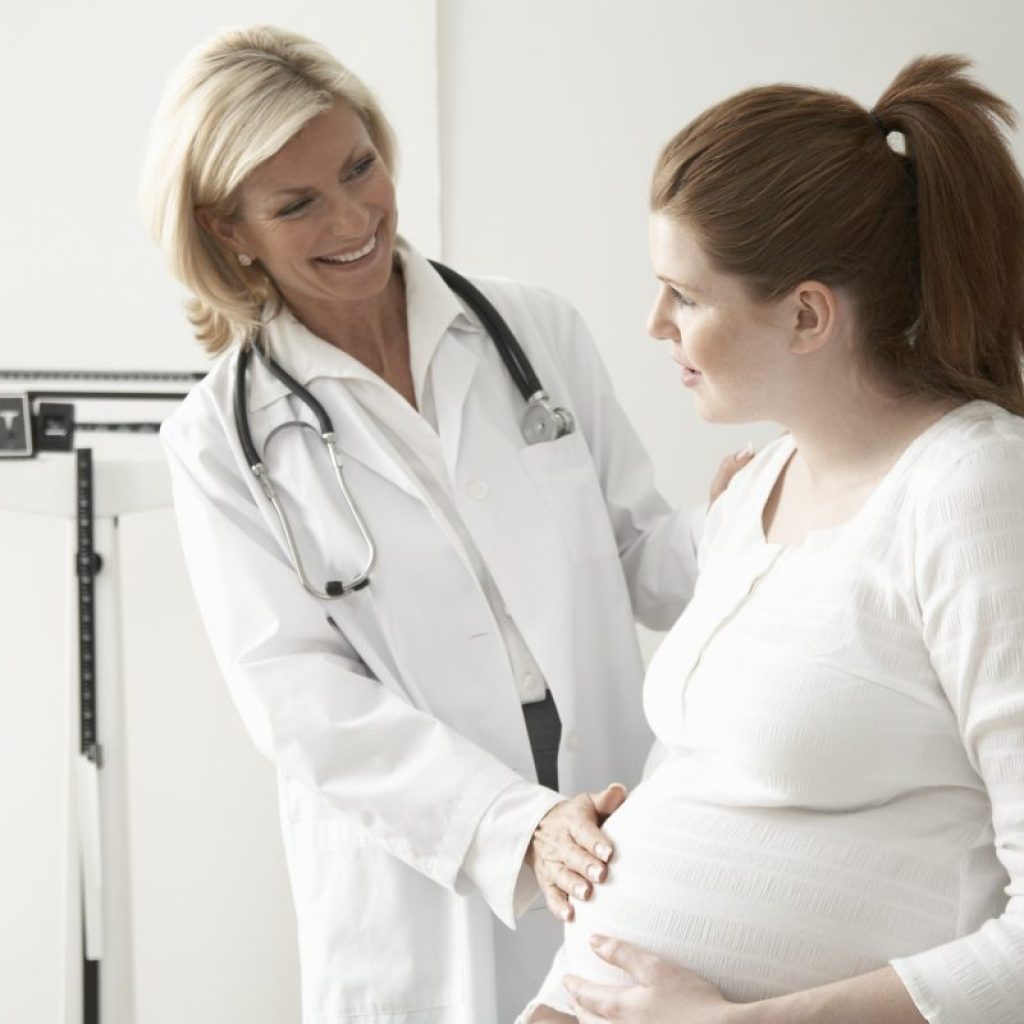 Female doctor touching pregnant woman's stomach, smiling