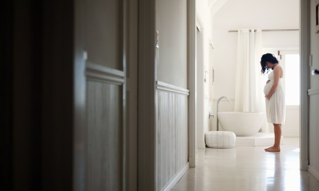 A pregnant woman holding her belly in a bathroom
