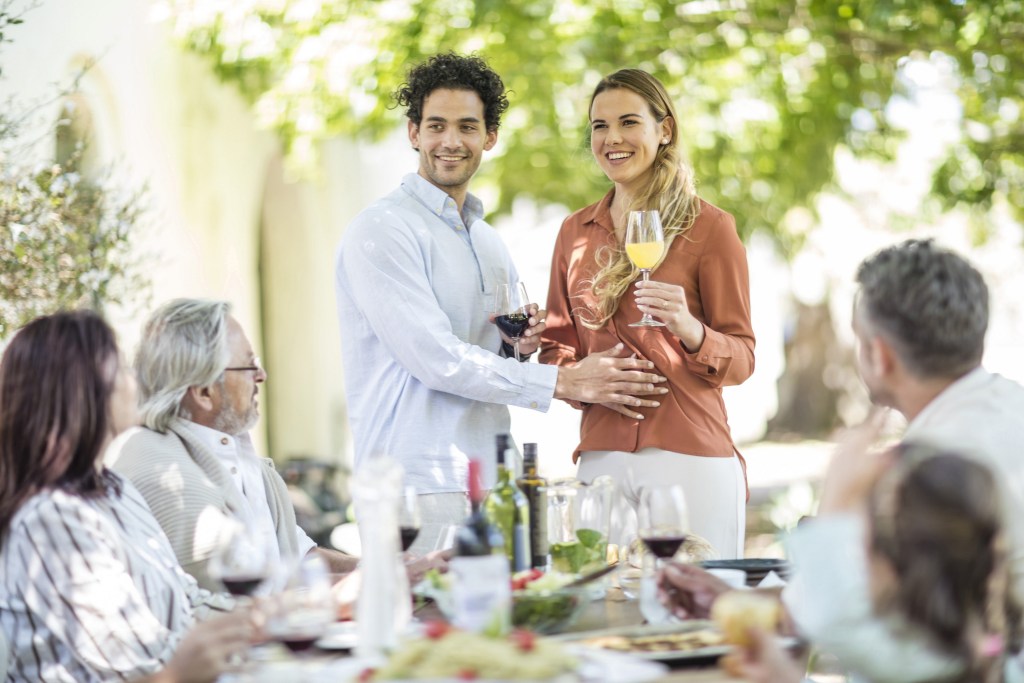 Young couple raising a toast with announcement of pregnancy to family during outside family lunch