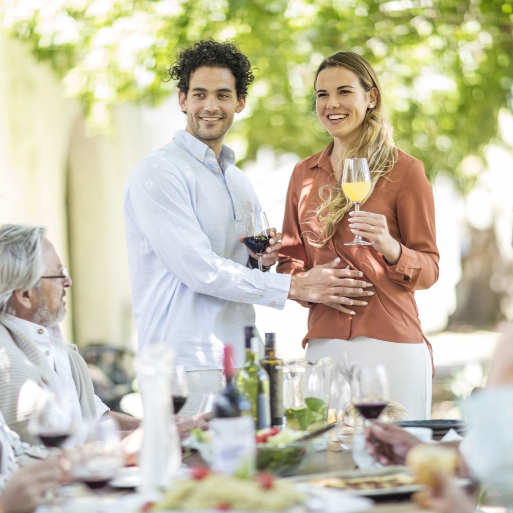 Young couple raising a toast with announcement of pregnancy to family during outside family lunch