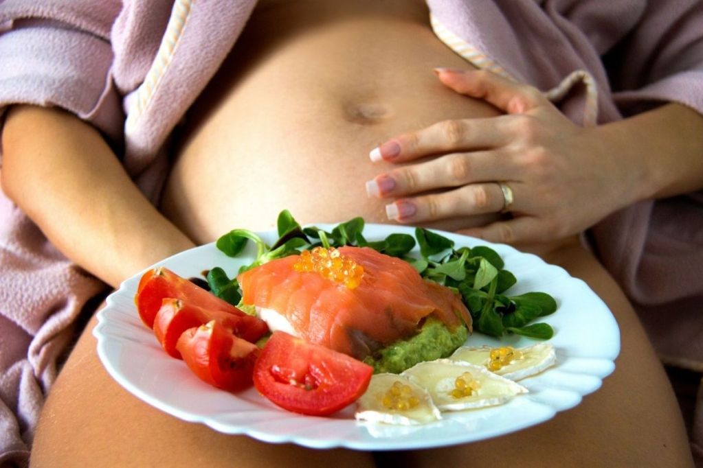 Pregnant person holding plate of healthy dinner over their bare bump
