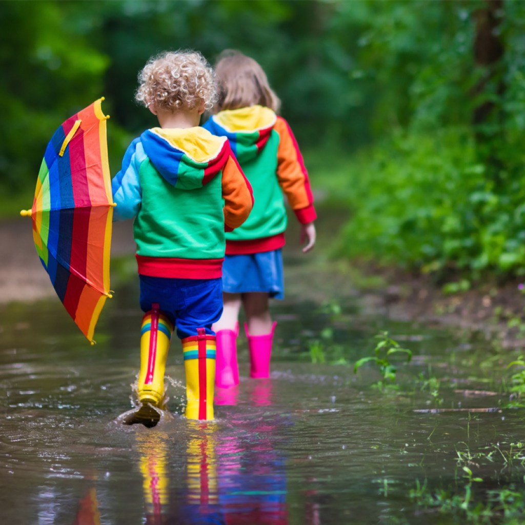 two toddlers walking through a large puddle in their rain boots