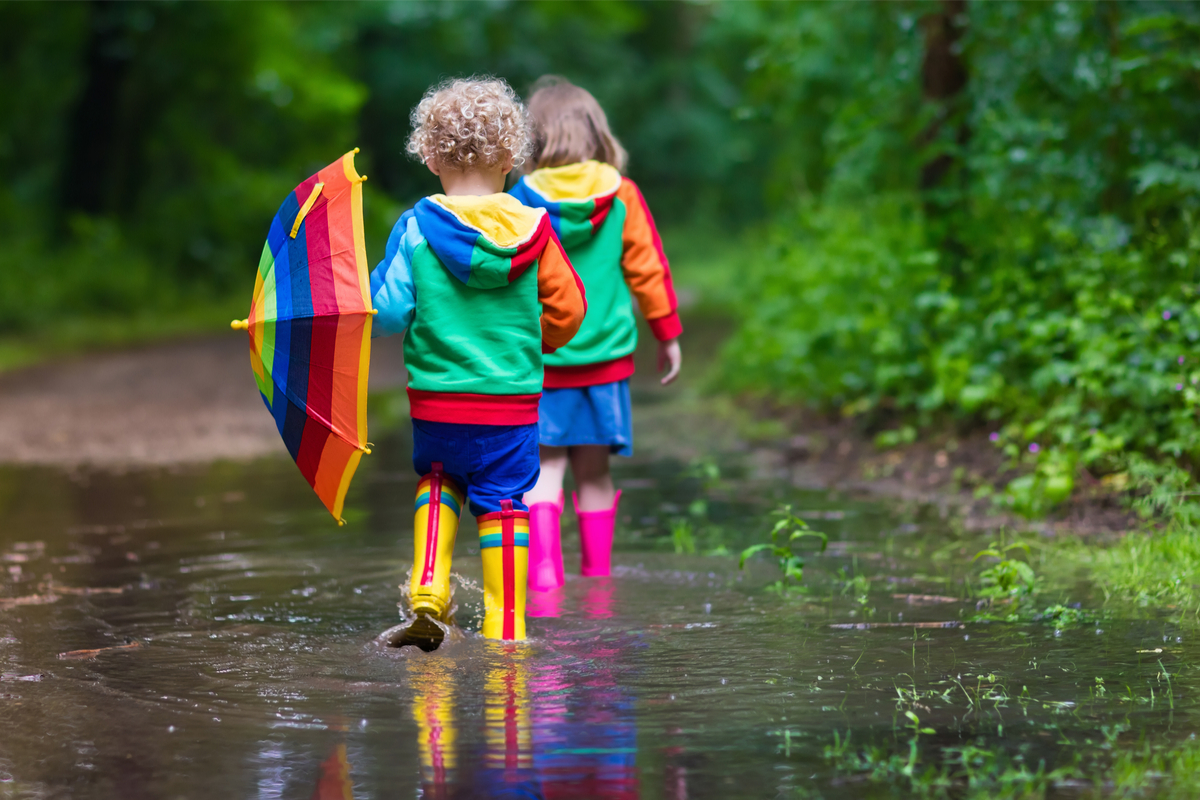 two toddlers walking through a large puddle in their rain boots