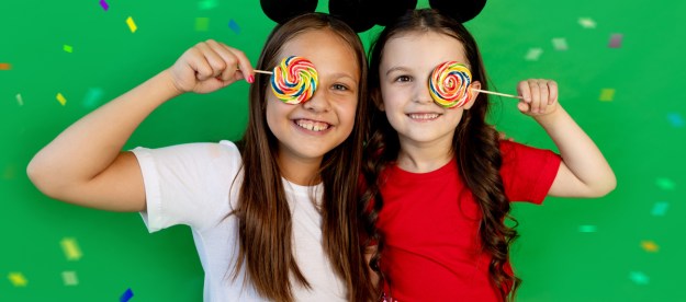 Two girls wearing Mickey ears holding suckers.