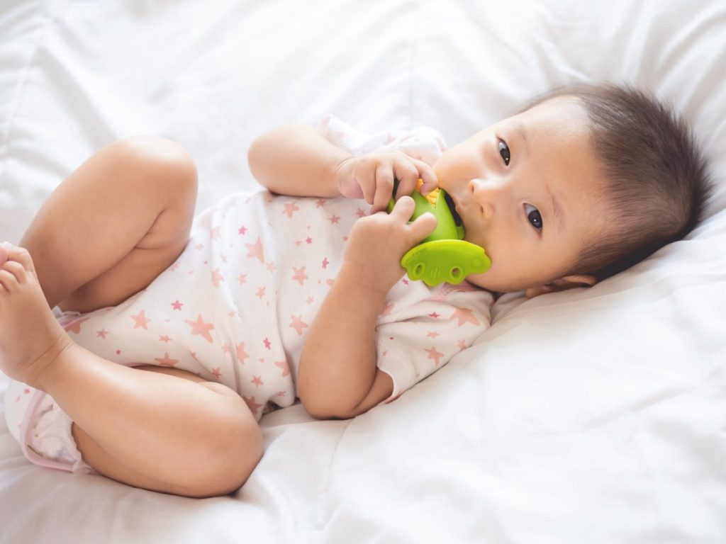 A teething baby in a onesie chewing on a teething toy