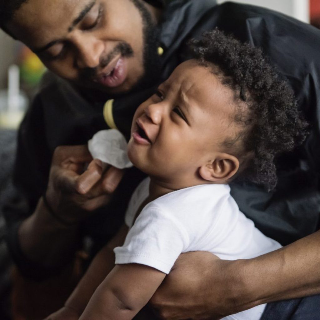 A father wiping a fussy baby's nose.
