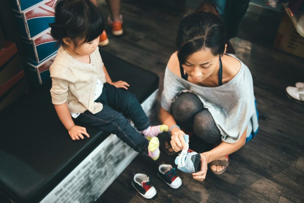 A mother trying shoes on her small child.