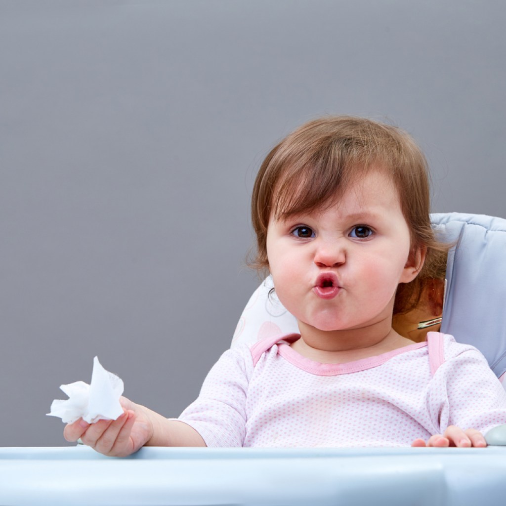 A little child holding a tissue in their hand and crinkling their face up.