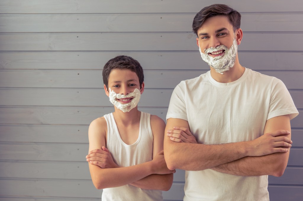 A father and son with shaving cream on their faces getting ready to shave.