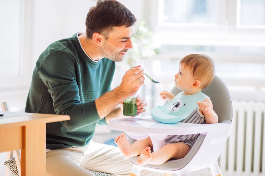 A parent feeding their baby food while the baby wears a bib.