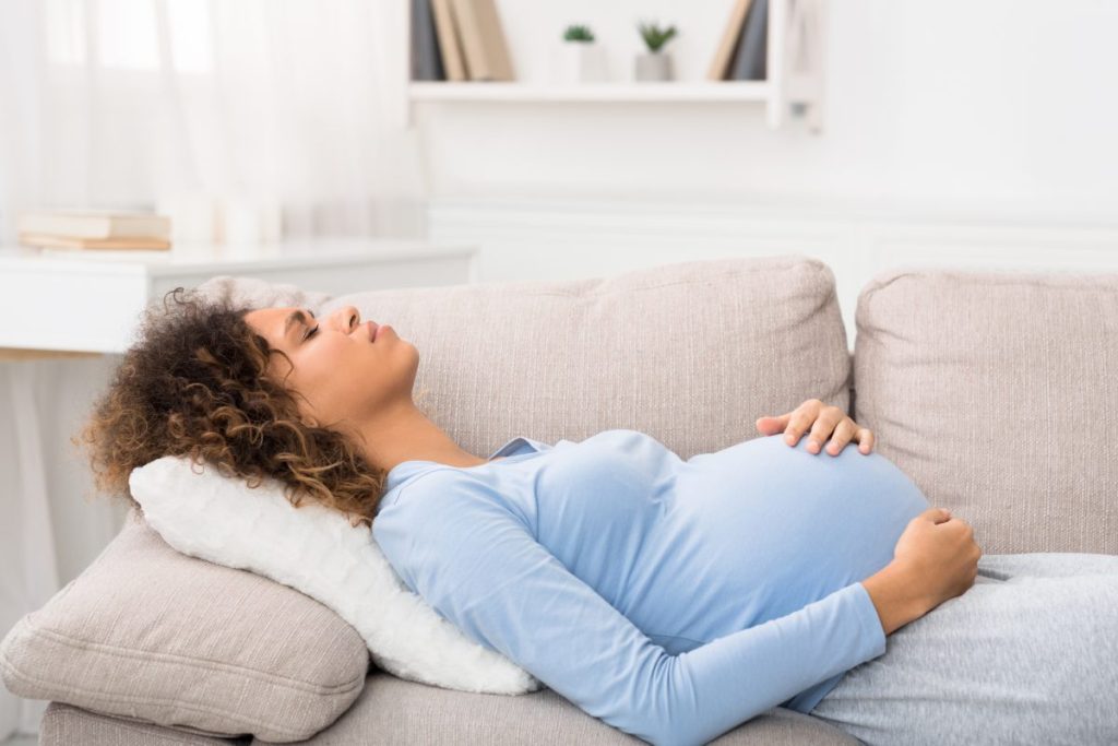 A pregnant woman lying on the couch holding her stomach