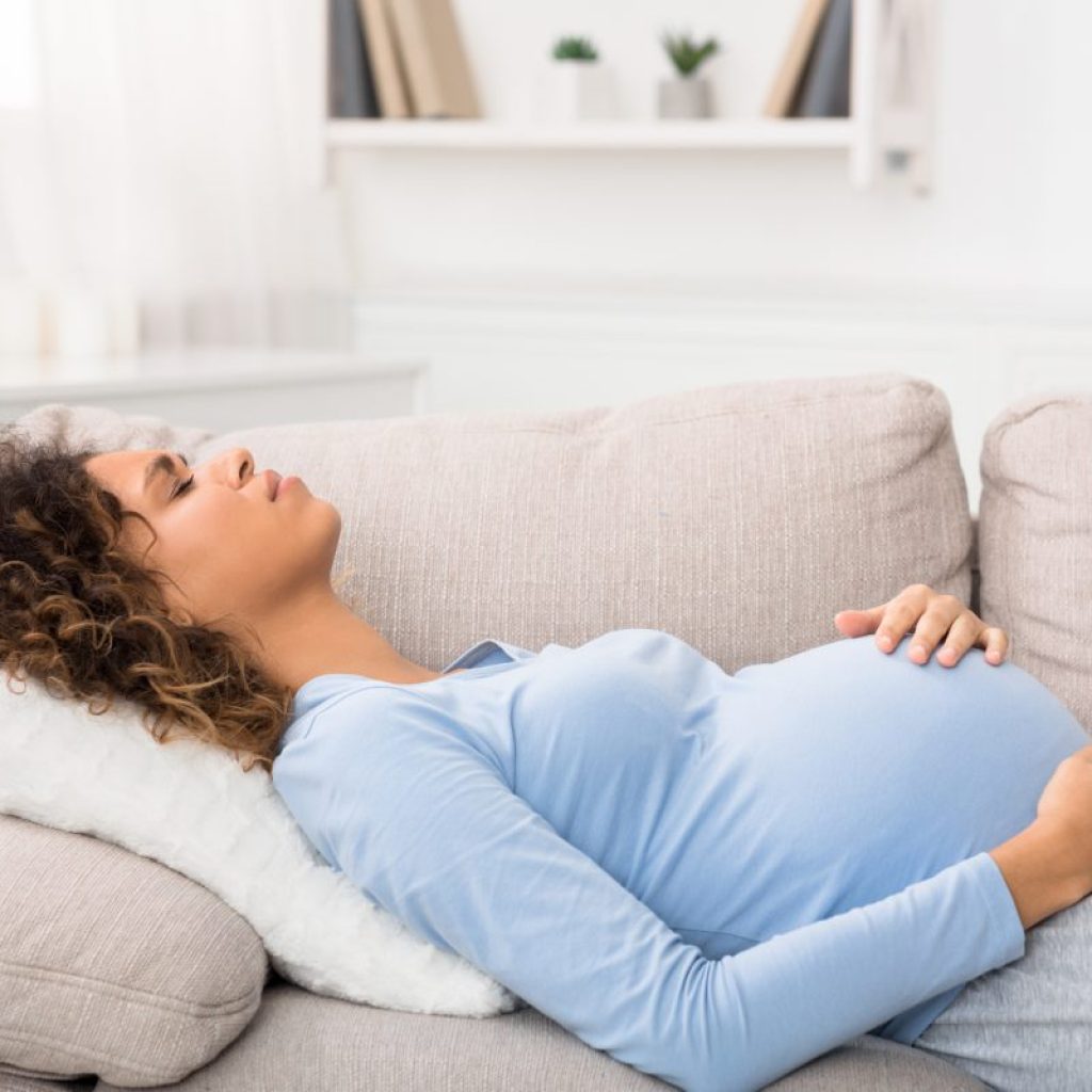 A pregnant woman lying on the couch holding her stomach