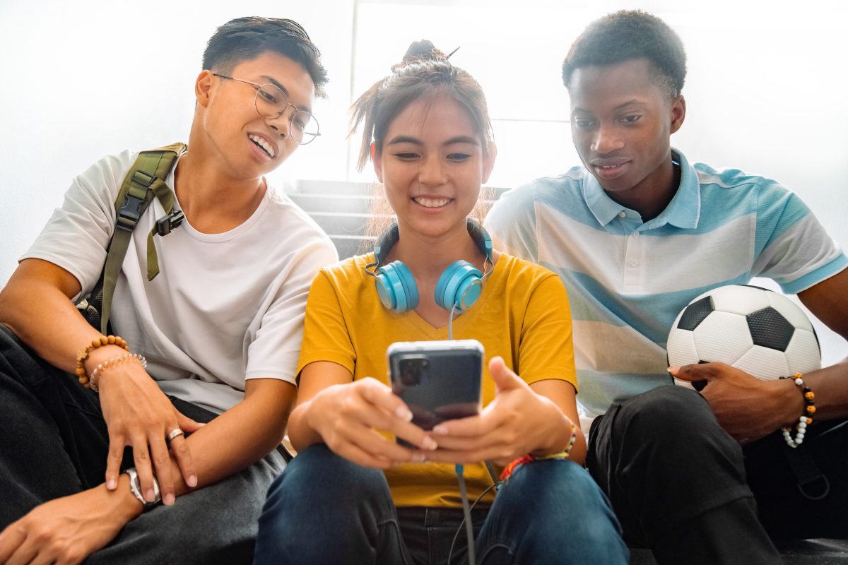 A group of teens looking at a cellphone.
