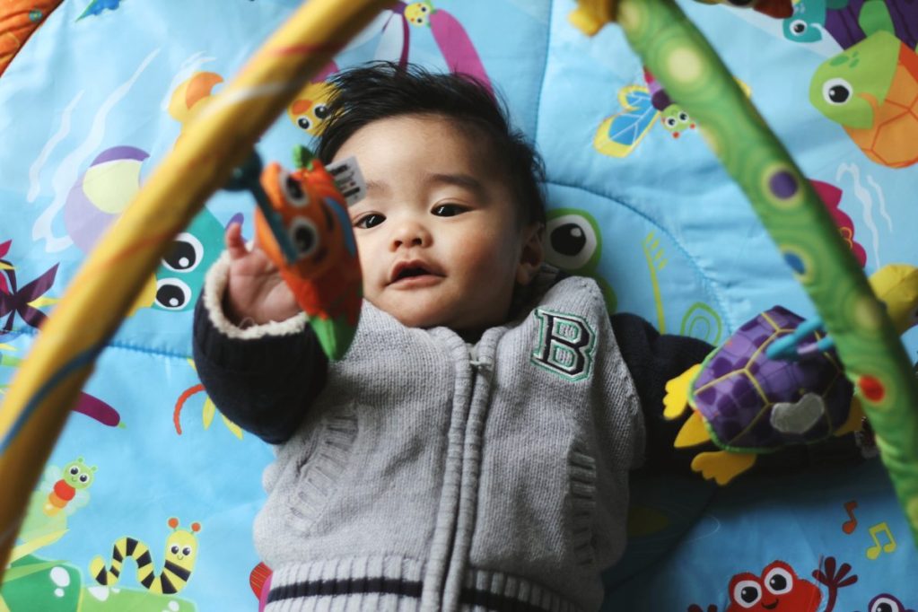 A baby on a play mat trying to get the dangling toys.