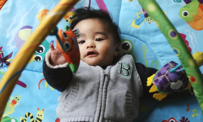 A baby on a play mat trying to get the dangling toys.