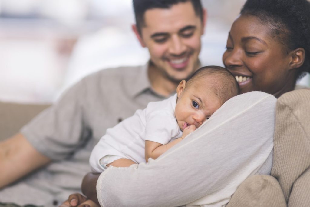 A mother holding her newborn baby with her partner looking on