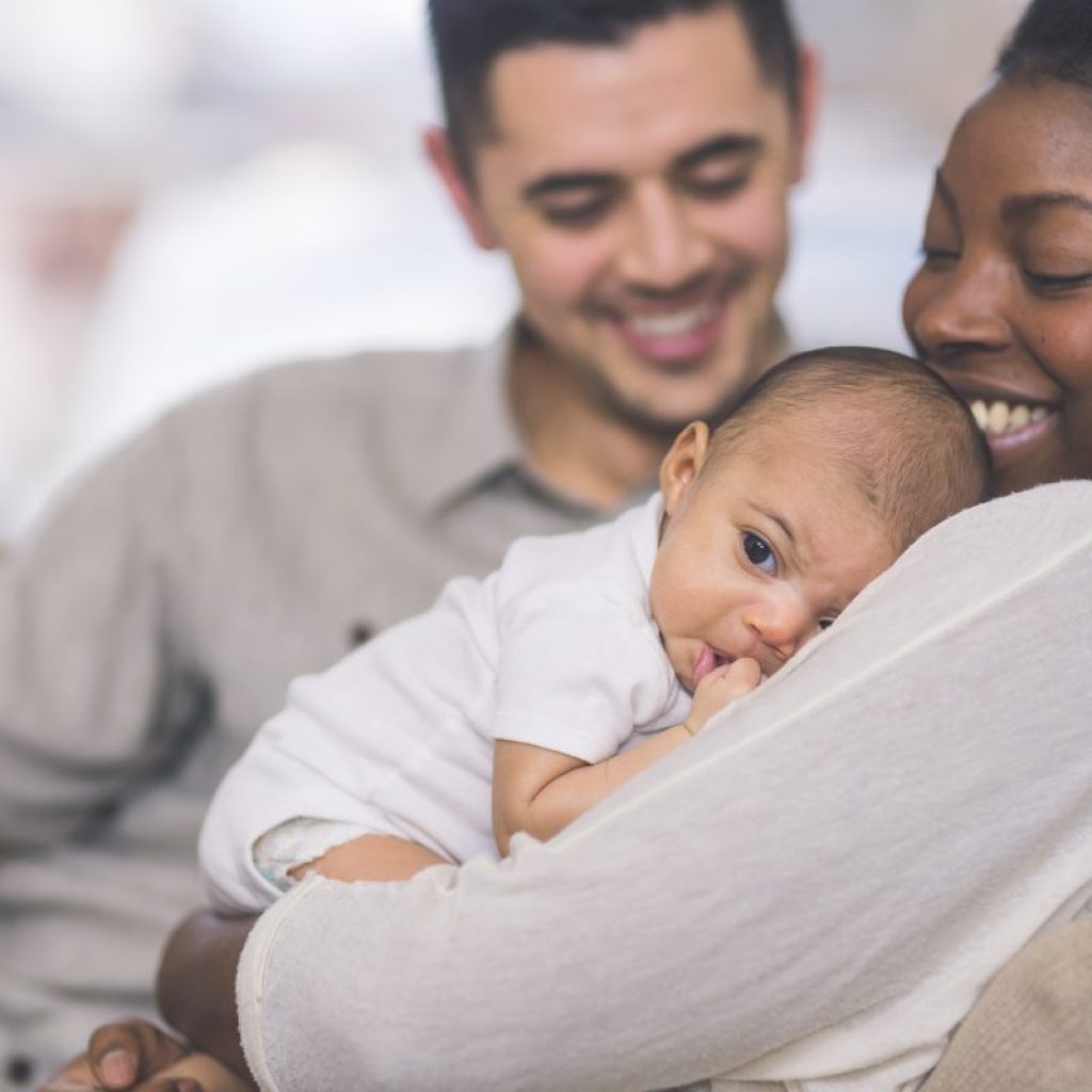 A mother holding her newborn baby with her partner looking on
