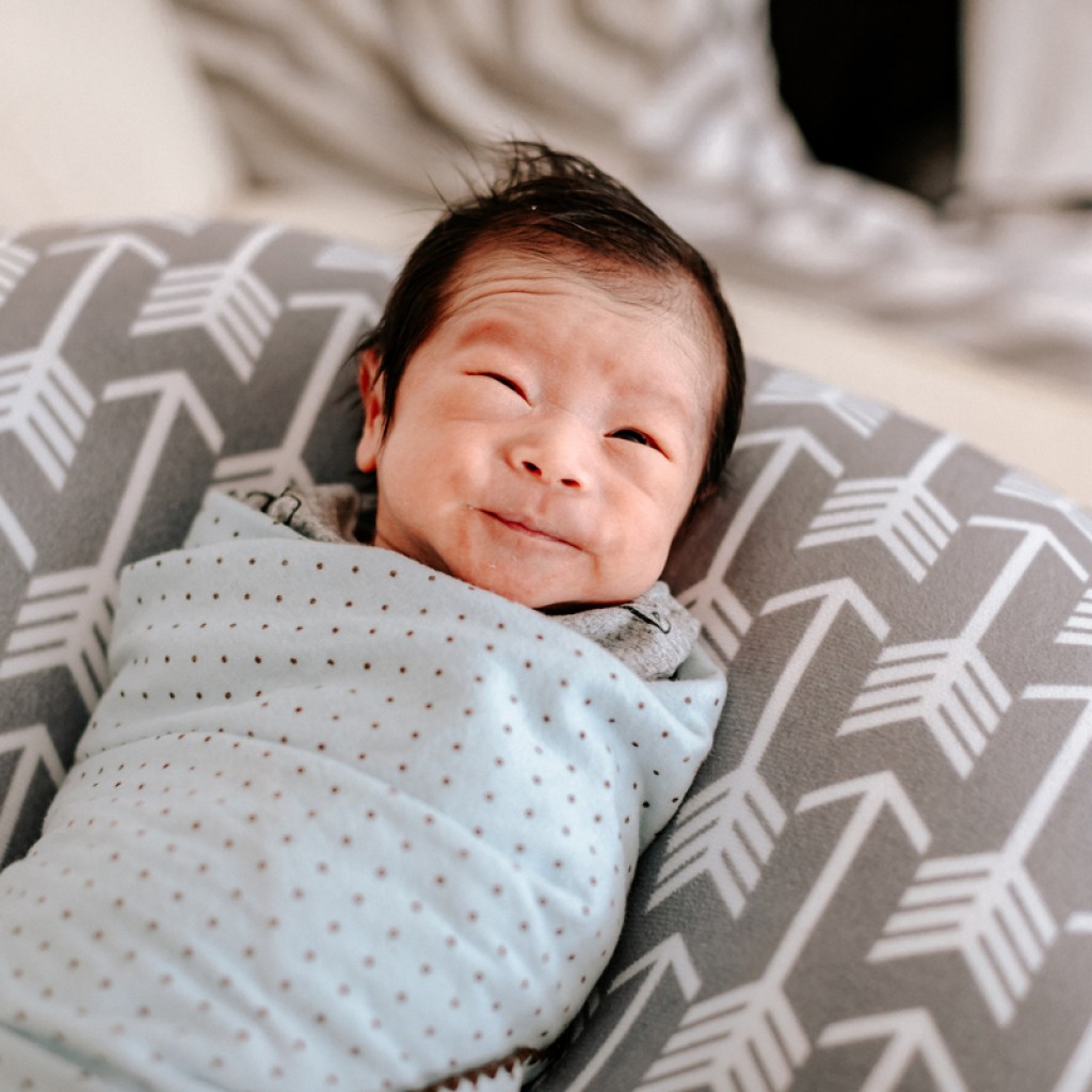 A swaddled baby supported by a pillow.