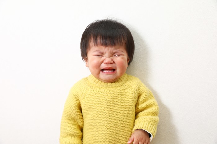 A toddler wearing a yellow sweater crying with their eyes closed.