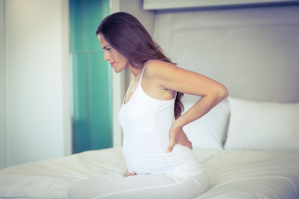 A pregnant woman having pains and holding her back.