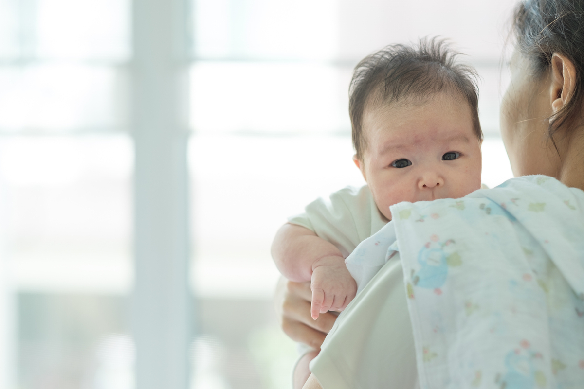 A parent holding a little baby over their shoulder.