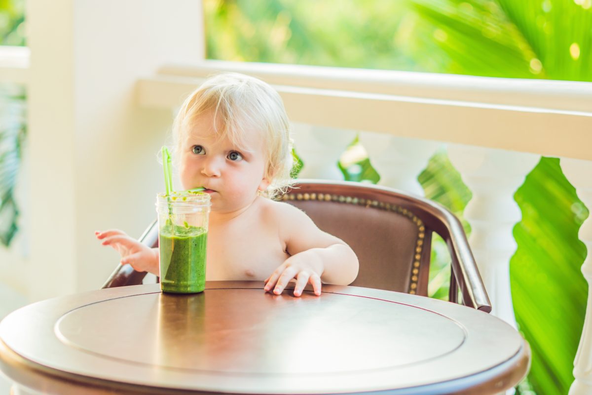 A baby drinking a green drink.