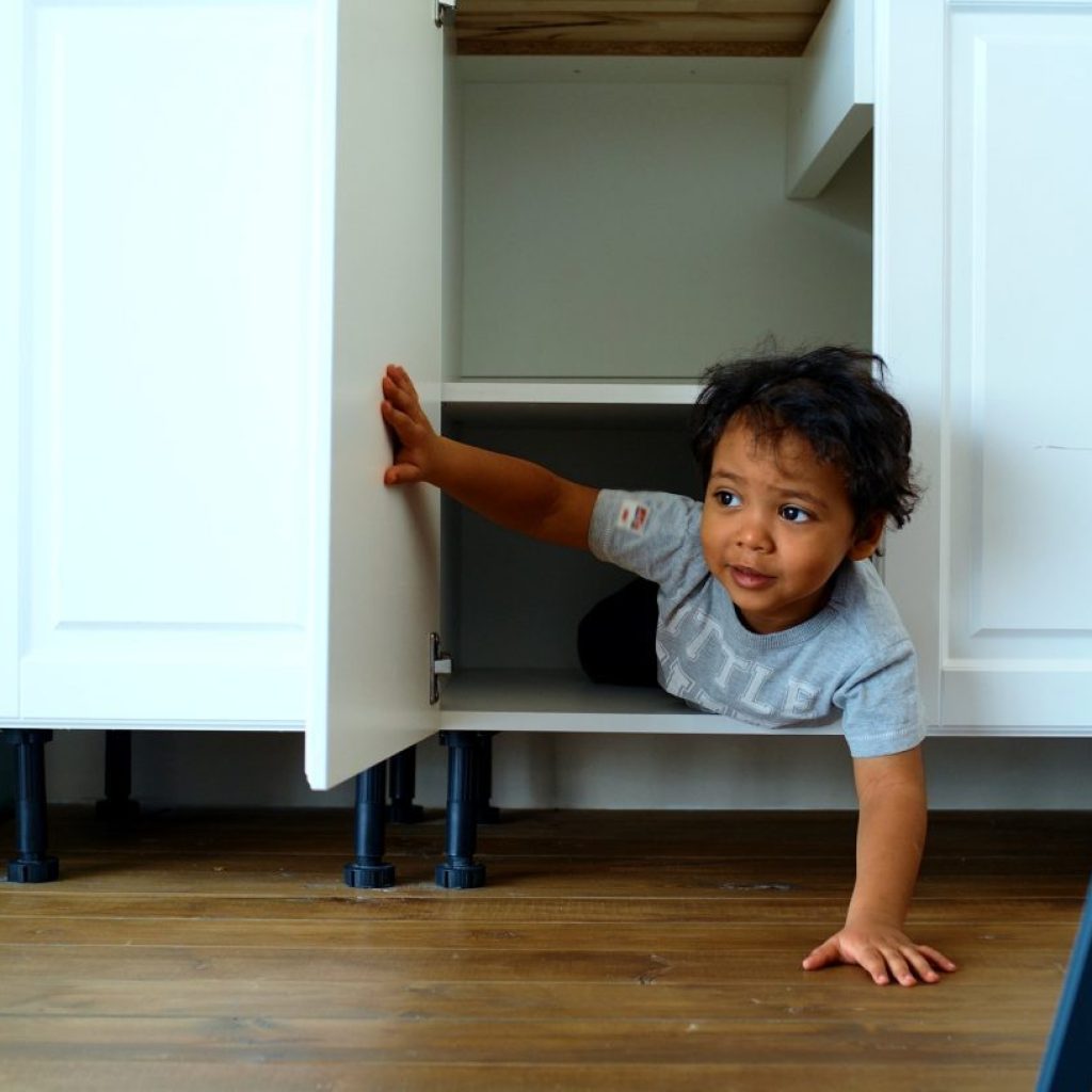 A little toddler boy playing hide and seek in a cabinet.