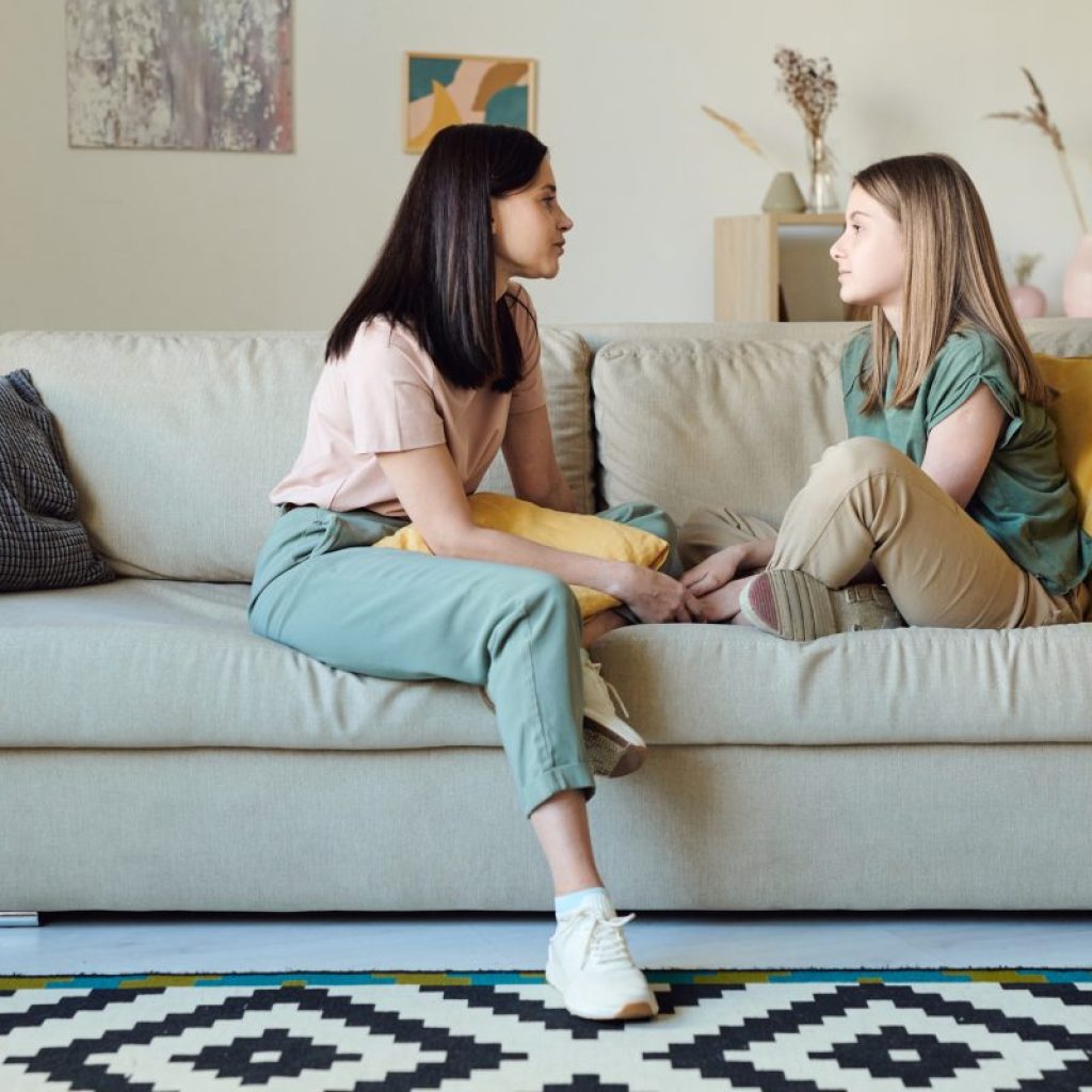 A mother and daughter having a conversation while sitting on the couch together.