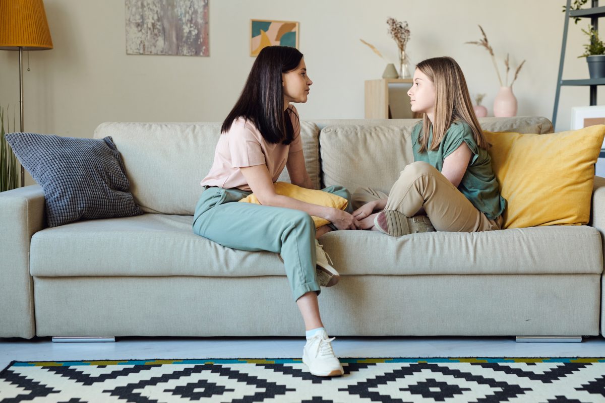 A mother and daughter having a conversation while sitting on the couch together.
