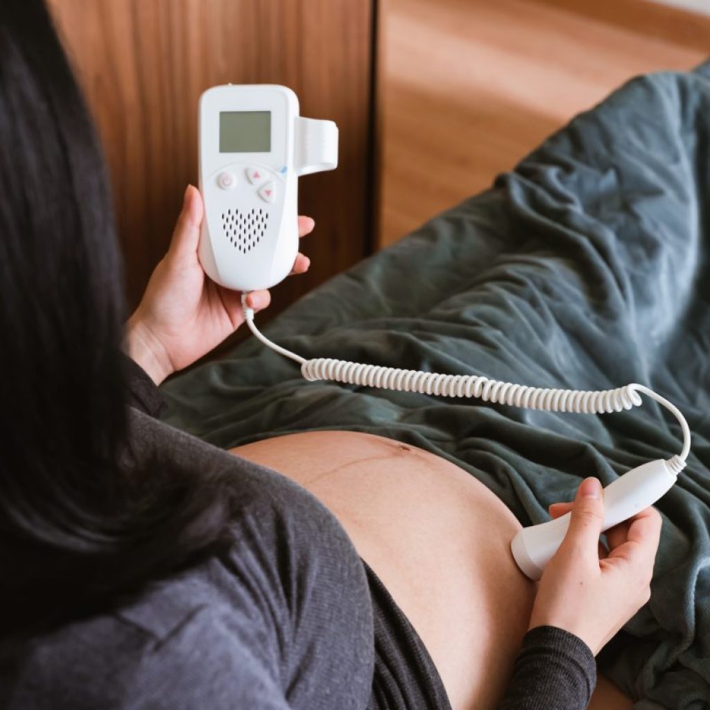 A pregnant woman using a monitor on her belly at home.