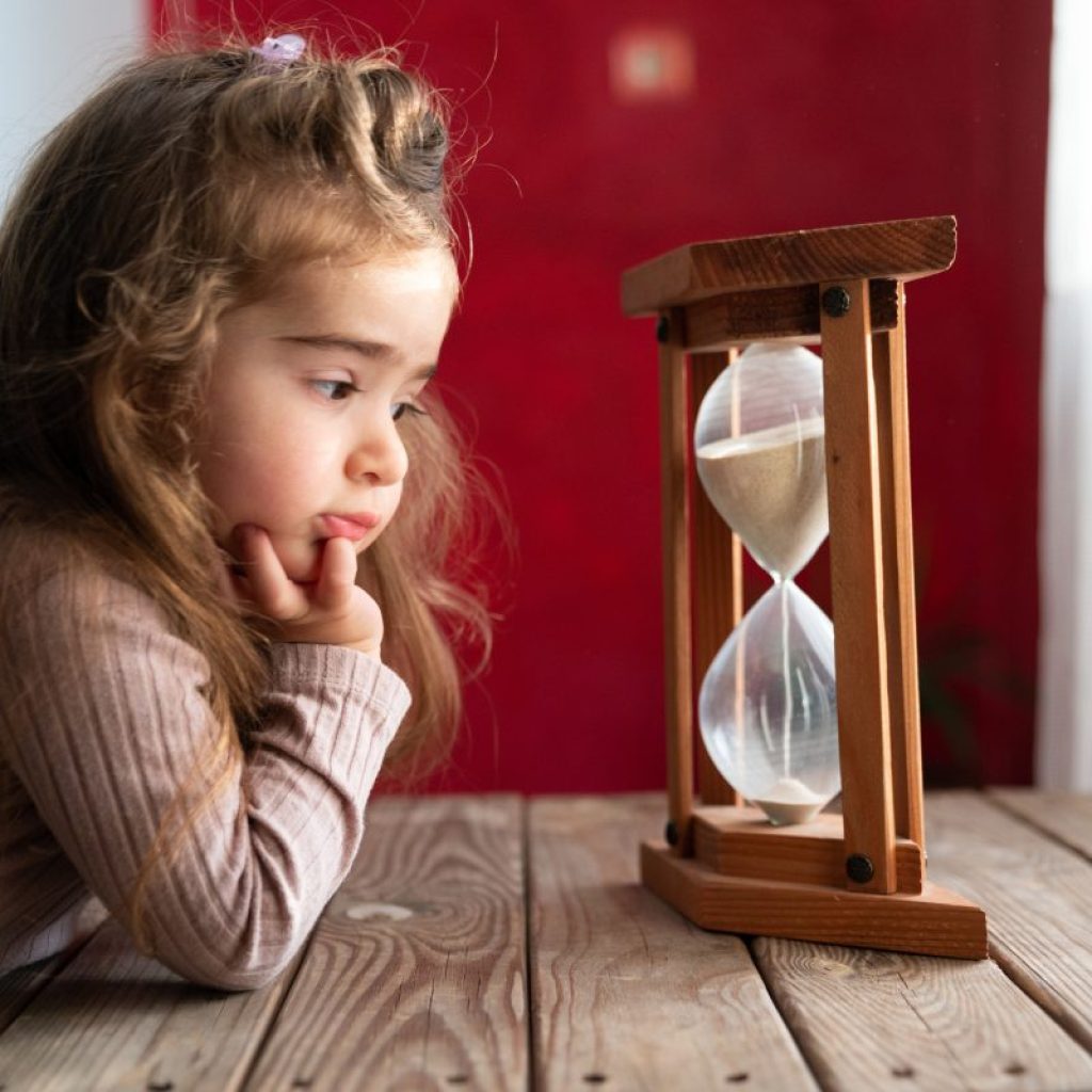A toddler girl looking at an hourglass pass time.