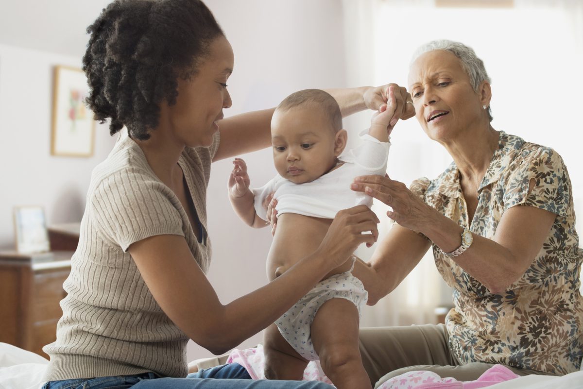 A mother and grandparent helping to dress a baby for the day.