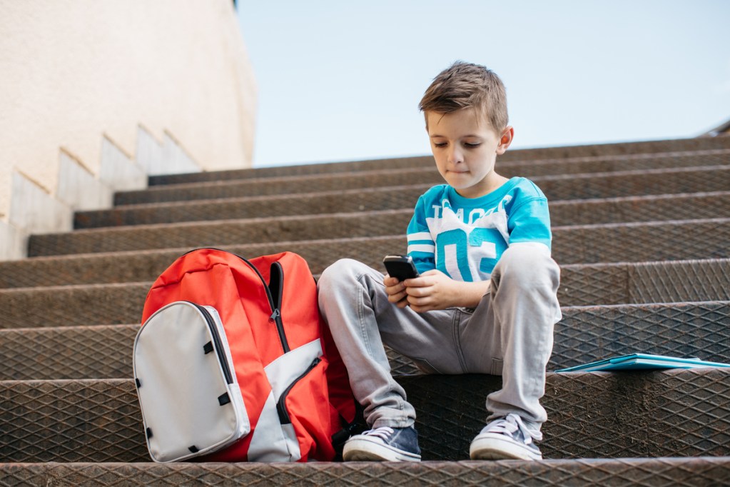 Boy texting mom after school on his cellphone.
