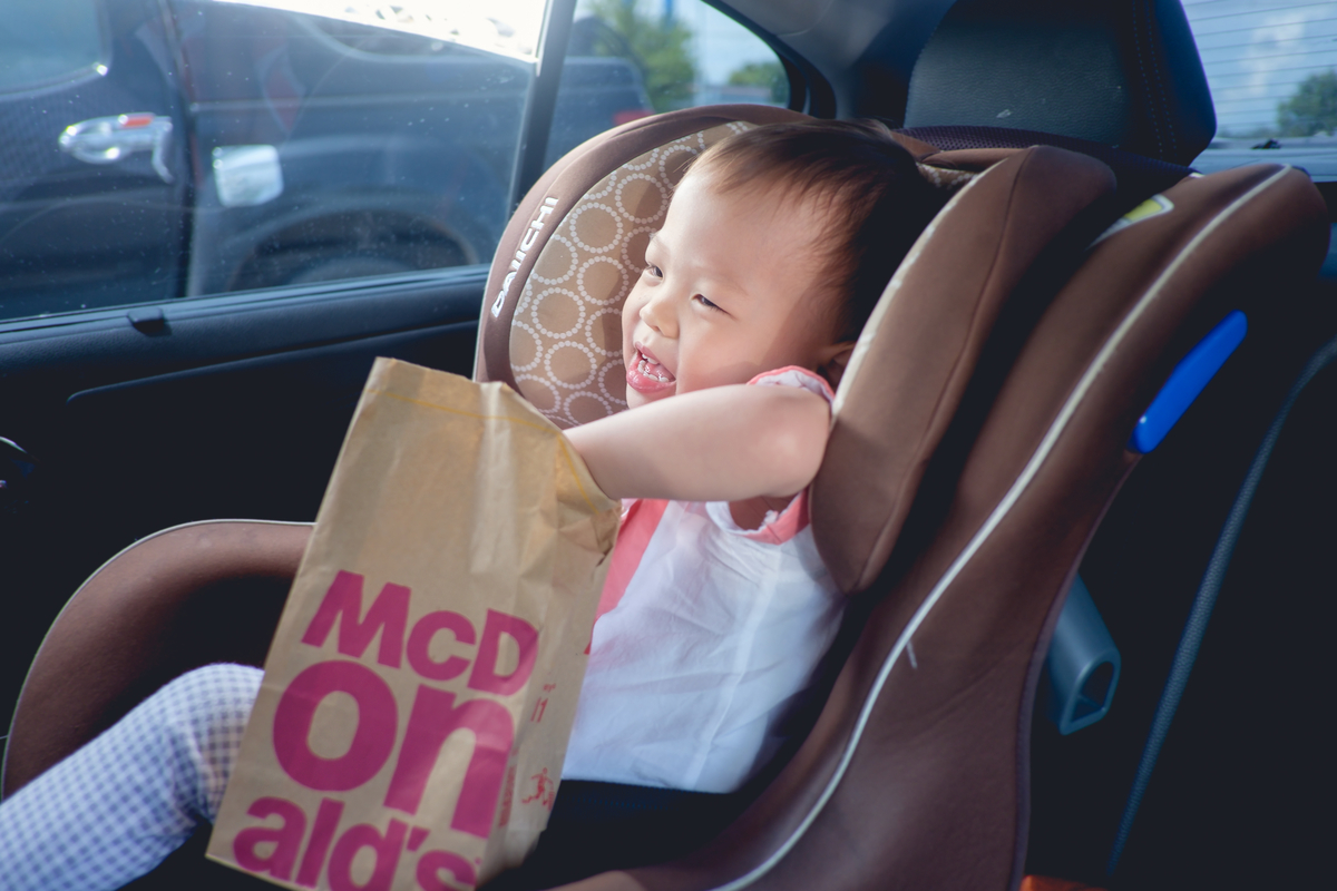A toddler reaching into a bag of fast food in the car